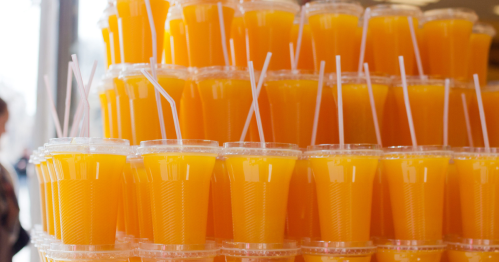 A stack of clear cups filled with bright orange juice, each topped with a straw.