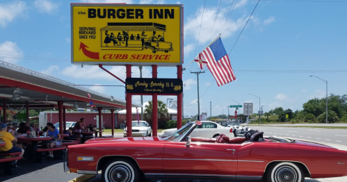 A red convertible parked outside the Burger Inn, featuring a bright sign and outdoor seating with diners.