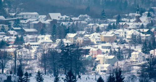 A snowy landscape featuring a cluster of houses and trees, with a backdrop of a wintery town.