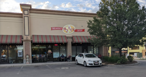 Exterior of a breakfast eatery with a sign, outdoor seating, and a white car parked in front.