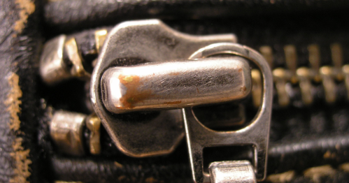 Close-up of a metallic zipper, showcasing the slider and teeth against a black background.