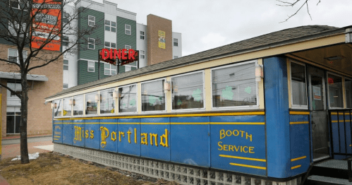 A blue diner with "Miss Portland" signage, featuring large windows and a booth service design, set against a modern building.