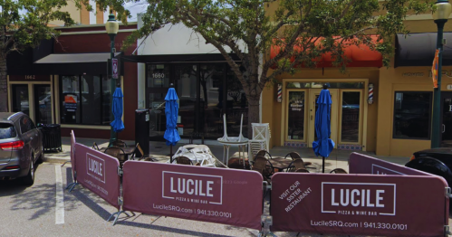 Outdoor dining area of Lucile Pizza & Wine Bar, featuring blue umbrellas and a fenced seating area.