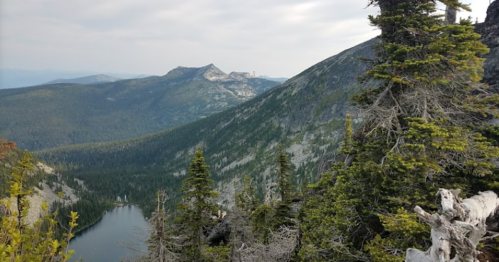 A scenic mountain landscape with lush greenery, rocky peaks, and a tranquil lake nestled in the valley below.