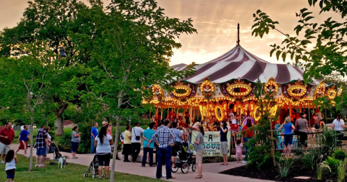 A vibrant carousel with colorful lights, surrounded by people enjoying a lively outdoor event at sunset.