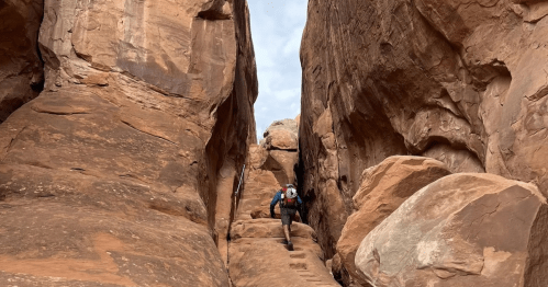 A hiker navigates a narrow canyon surrounded by towering rock formations.