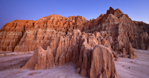 Stunning rock formations in warm hues at sunset, showcasing layered textures and dramatic cliffs in a desert landscape.