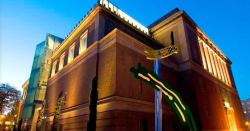 A modern building with a brick facade, illuminated at dusk, featuring abstract green and yellow designs.