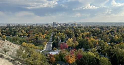 A panoramic view of a city skyline surrounded by vibrant autumn trees and a cloudy sky.