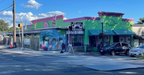 Colorful building with pink and green exterior, featuring a sign for Claire's Beach Shack and palm tree murals.