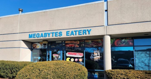 Exterior of Megabytes Eatery, featuring a sign and large windows displaying food images. Bushes in front.