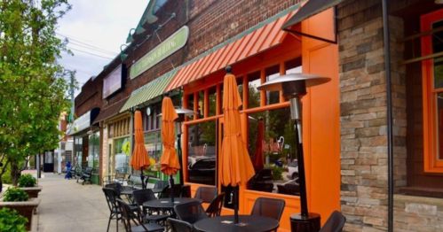 Outdoor seating area with orange umbrellas in front of a brick building, featuring large windows and a cozy atmosphere.