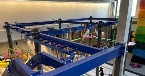 Indoor climbing structure with blue beams, ropes, and platforms, designed for recreational activities.