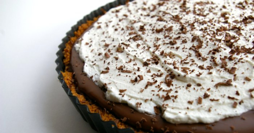 A close-up of a chocolate cream pie topped with whipped cream and chocolate shavings in a black pie crust.