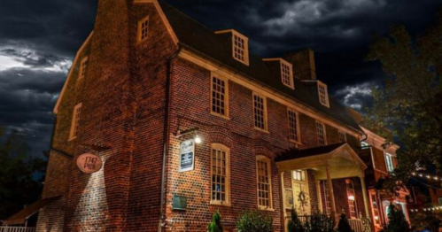 A historic brick building with multiple windows, illuminated under a dark, cloudy sky.