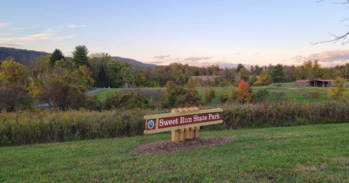 Sign for Sweet Run State Park in a scenic landscape with trees and mountains in the background during sunset.
