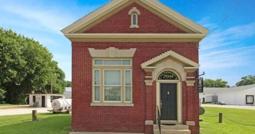 A red brick building with a decorative entrance, surrounded by green grass and trees under a clear blue sky.