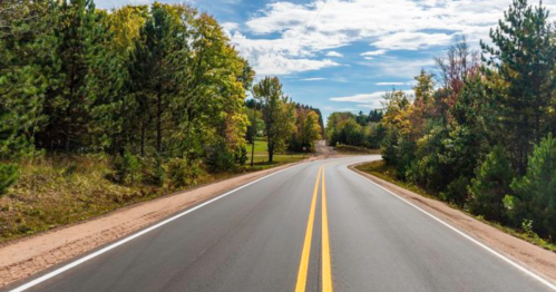 A winding road surrounded by trees under a blue sky with scattered clouds.