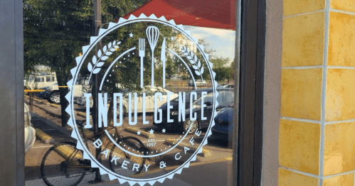 Logo of "Indulgence Bakery & Café" displayed on a window, featuring utensils and decorative elements.