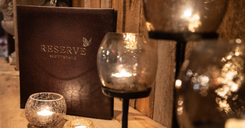 A dimly lit setting featuring a menu titled "Reserve Scottsdale" and decorative candle holders with flickering candles.