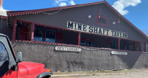 Exterior of the Mine Shaft Tavern, a rustic restaurant with a red jeep parked in front and blue skies above.