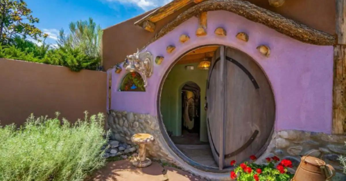 Whimsical round door of a colorful adobe-style home, surrounded by greenery and flowers.