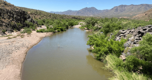 A winding river flows through a rocky landscape, surrounded by lush greenery and mountains in the background.