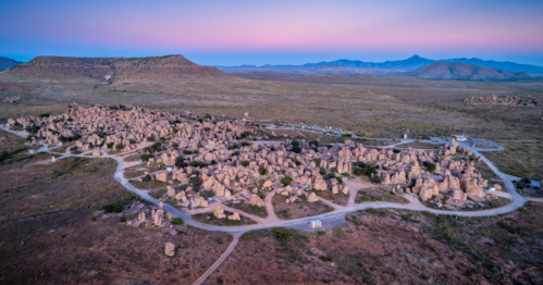 Aerial view of a vast landscape with numerous stone formations and winding paths under a pastel sky at dusk.