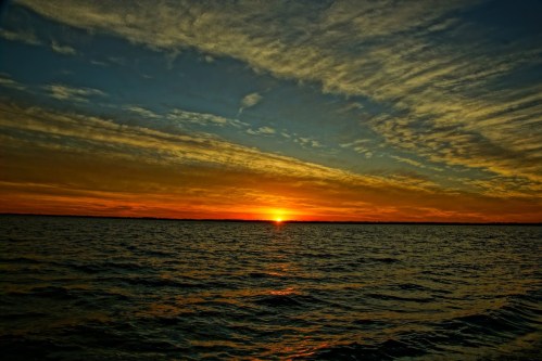 A vibrant sunset over calm waters, with colorful clouds reflecting the warm hues of the sky.
