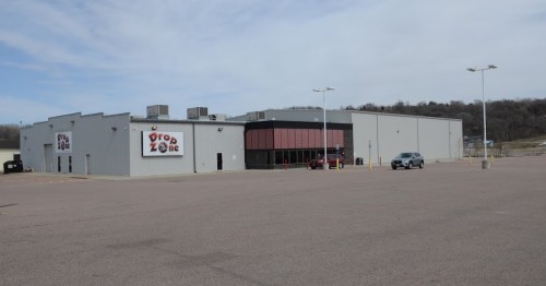 A large, gray commercial building with a red-accented entrance, surrounded by an empty parking lot.