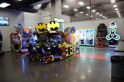 A brightly lit arcade featuring various games, including Batman-themed machines and colorful prize games.