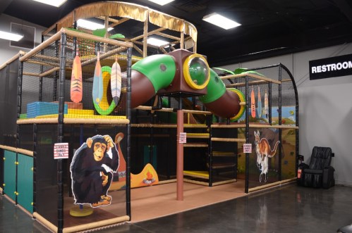 Indoor play structure featuring colorful slides, tunnels, and animal-themed decorations. Restroom sign visible in background.