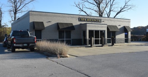 A gray building with the sign "Spa Bilanca," featuring black awnings and a parking lot with a truck nearby.