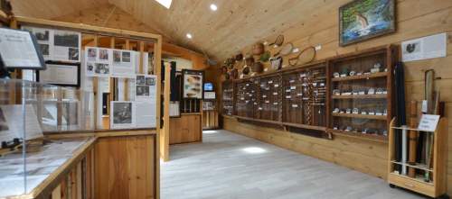 Interior of a wooden museum exhibit featuring displays of artifacts, photographs, and information panels.