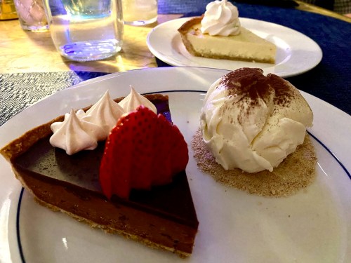 A plate with two desserts: a chocolate pie topped with strawberries and a slice of cream pie with whipped cream.