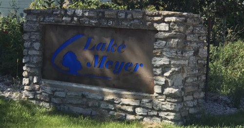 Sign for Lake Meyer, featuring blue lettering on a stone structure surrounded by greenery.