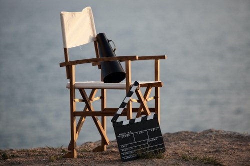 A director's chair and a clapperboard sit by the water, evoking a film set atmosphere.