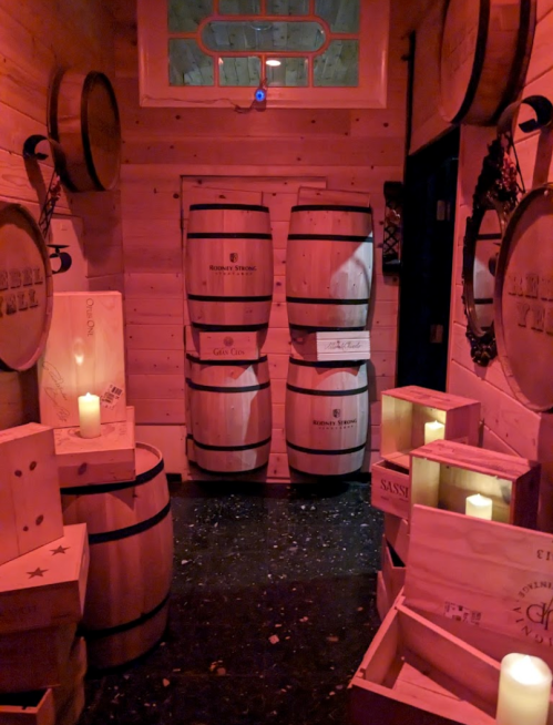A dimly lit room with wooden barrels and crates, creating a cozy, rustic atmosphere.