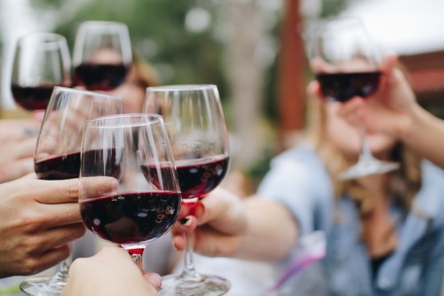 A group of people toasting with glasses of red wine outdoors, celebrating together.