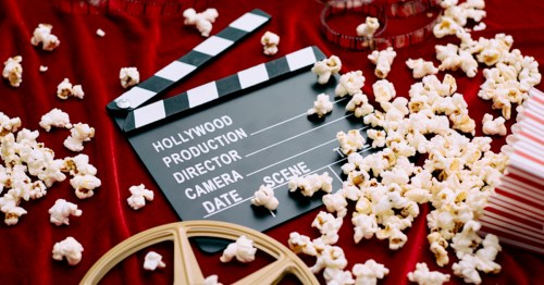 A film clapperboard surrounded by popcorn and film reels on a red velvet background.
