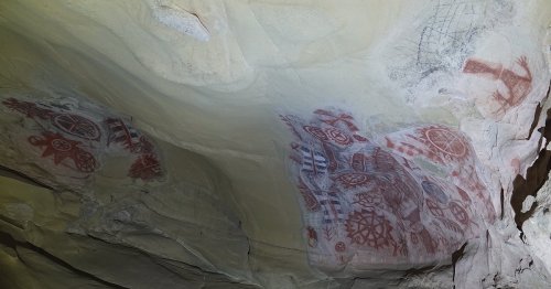 Ancient cave paintings on a rocky ceiling, featuring red and black geometric designs and symbols.