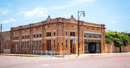 Historic brick building with decorative architecture, located on a street corner under a clear blue sky.