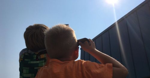 Two children looking up at the sky, shielding their eyes from the bright sun.