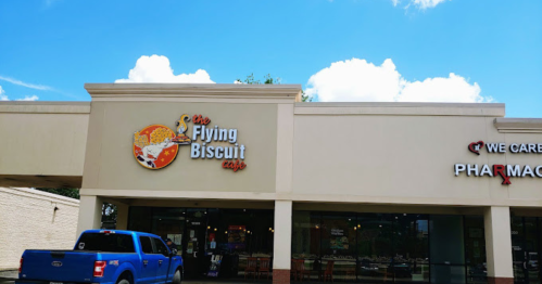 Exterior of The Flying Biscuit Cafe with a blue truck parked outside and a pharmacy sign nearby under a bright sky.