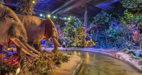 A lifelike elephant statue near a winding waterway, surrounded by vibrant, colorful foliage and ambient lighting.