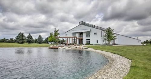 A modern building beside a pond, surrounded by greenery and cloudy skies.