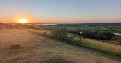 A serene landscape at sunset, featuring rolling hills, a river, and a vibrant sky with warm colors.