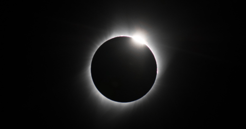 A solar eclipse with a dark circle surrounded by a glowing halo of light.