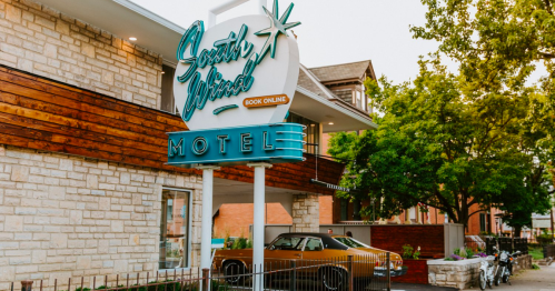Sign for South Wind Motel with retro design, surrounded by greenery and a classic car parked nearby.