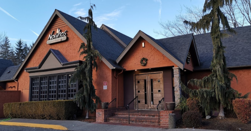 Exterior of a restaurant named "Noma's," featuring a warm orange facade, decorative wreath, and surrounding greenery.